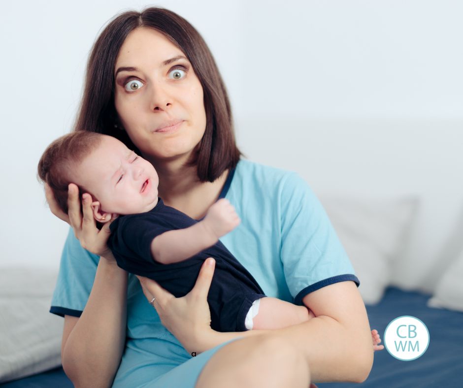 Mom holding a crying baby with an exasperated look on her face