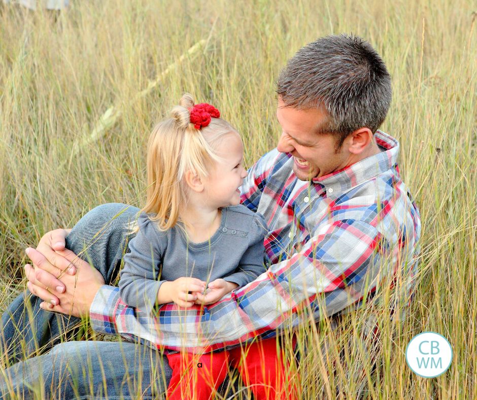 Brinley sitting on her dad's lap in a field