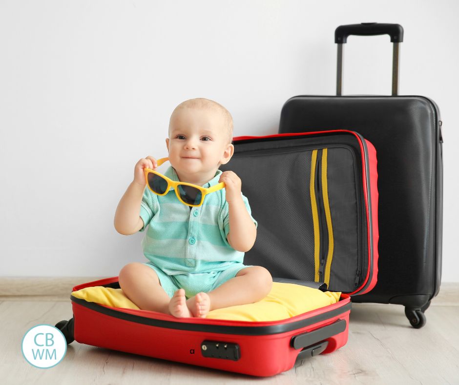 Baby sitting in an open suitcase holding sunglasses