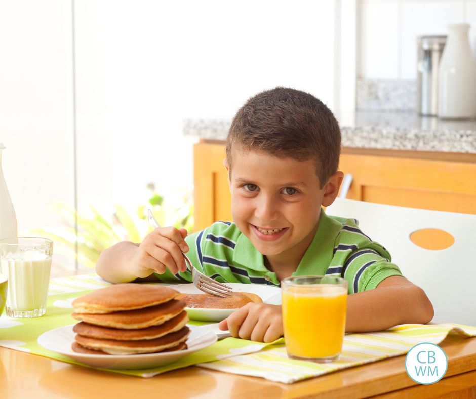 Boy eating pancakes and drinking orange juice.