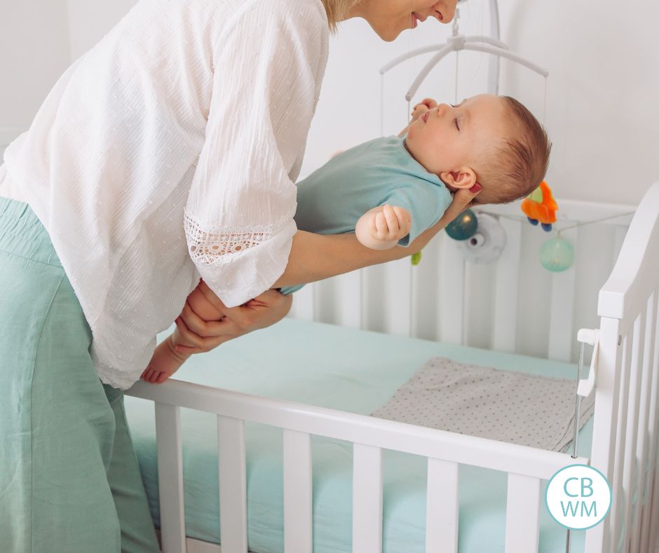 Mom putting a sleeping baby into the crib