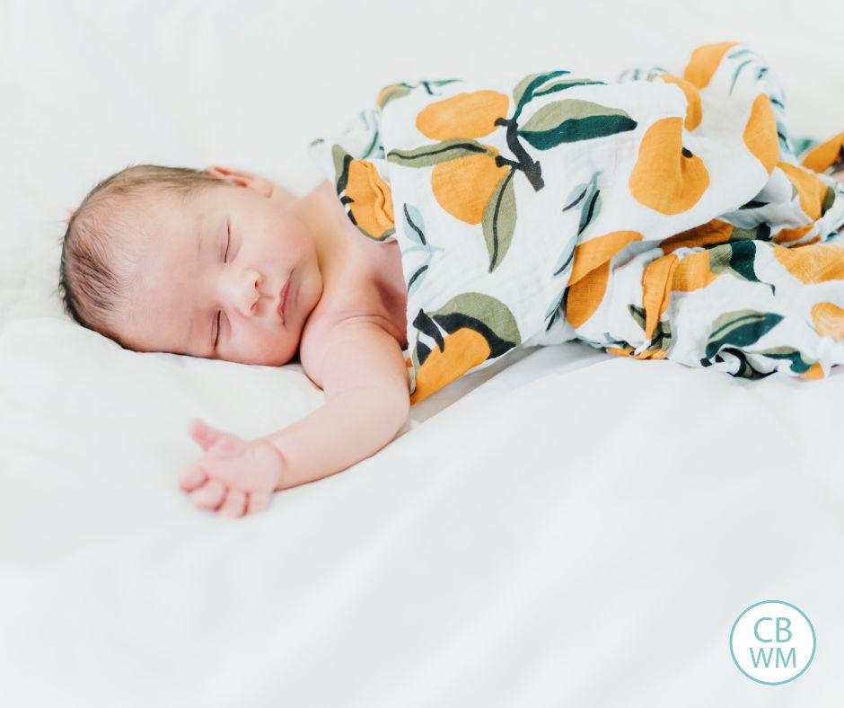 Baby sleeping wrapped up in a blanket with oranges on it