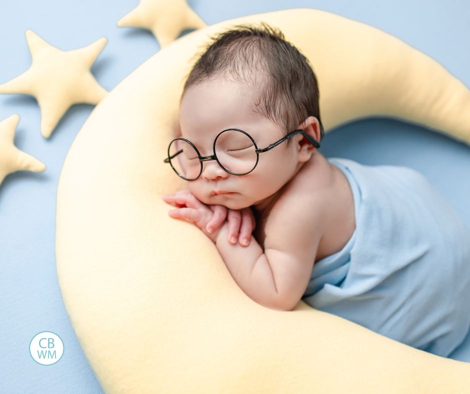 Baby sleeping on a stuffed moon wearing glasses