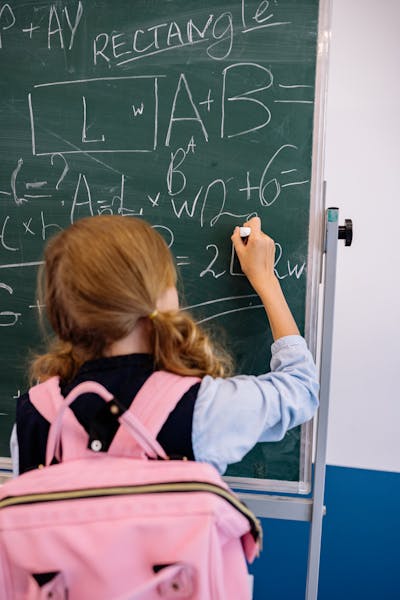 Child wearing a backpack and writing on the chalkboard