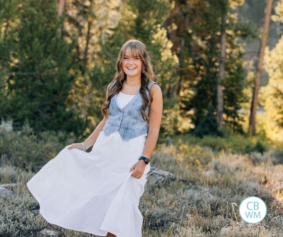 Kaitlyn wearing a white skirt and blue vest standing in the mountains