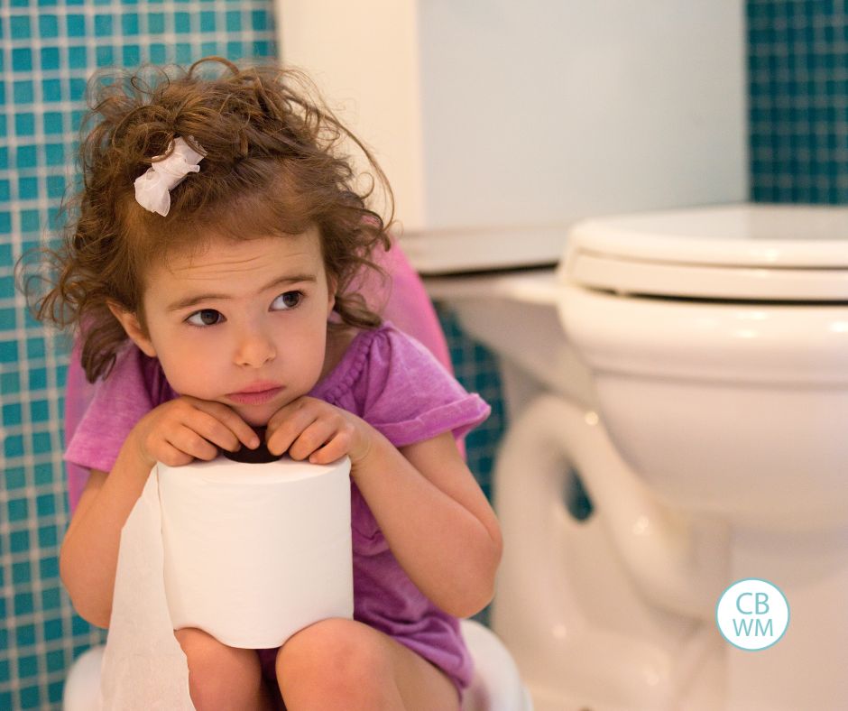 Girl sitting next to public toilet. She is cowering and looking nervous