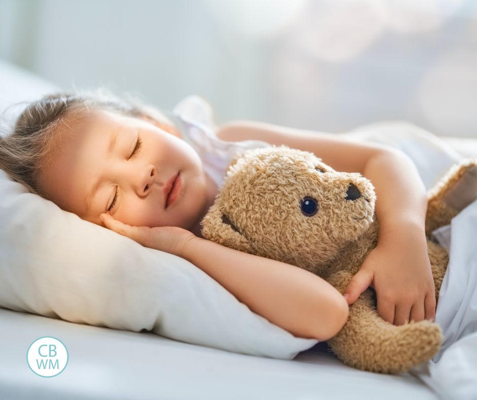 Child sleeping in bed hugging a teddy bear