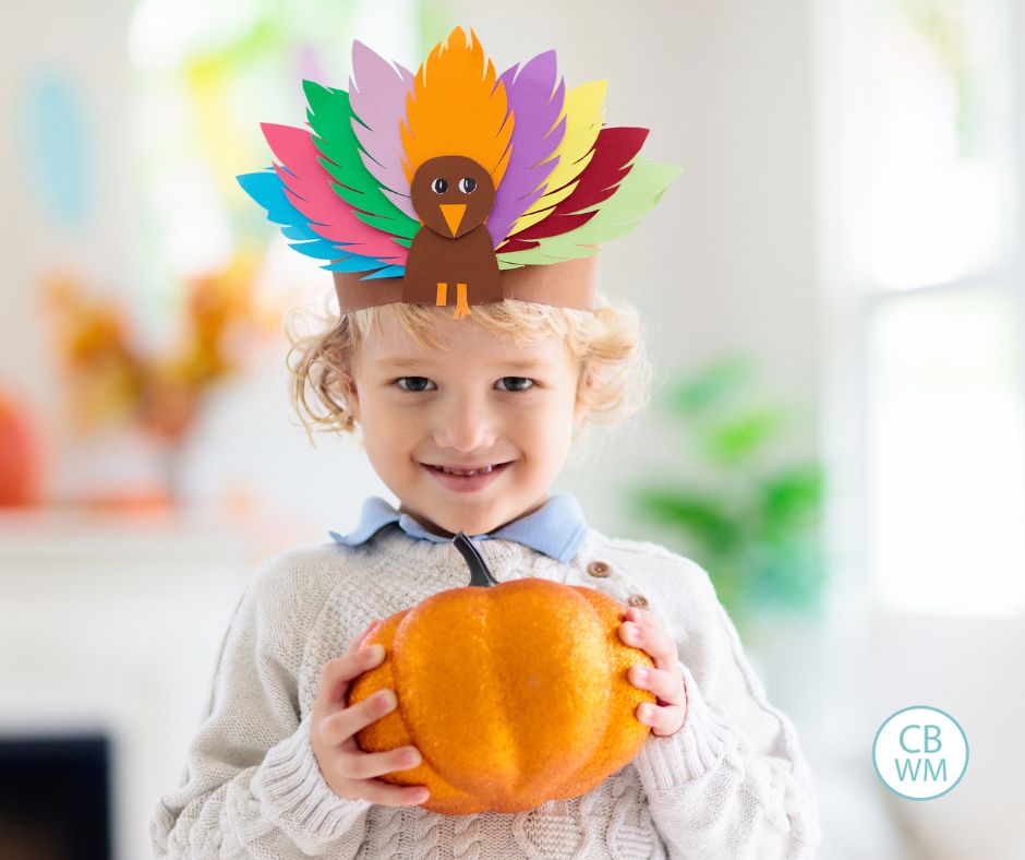Child wearing a turkey headband and holding a pumpkin