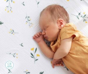 newborn baby wearing yellow sleeping on a muslin blanket