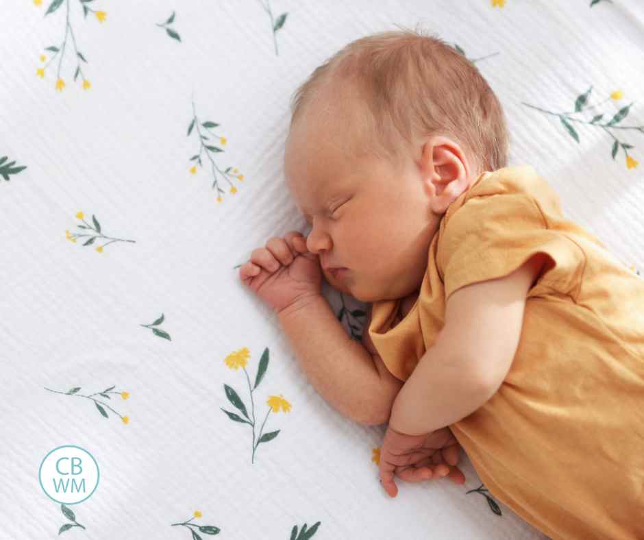 newborn baby wearing yellow sleeping on a muslin blanket