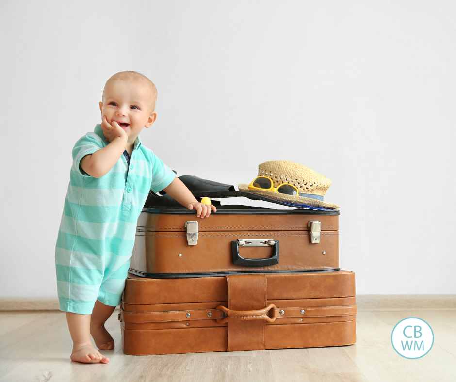 Baby standing next to a stack of brown suitcases