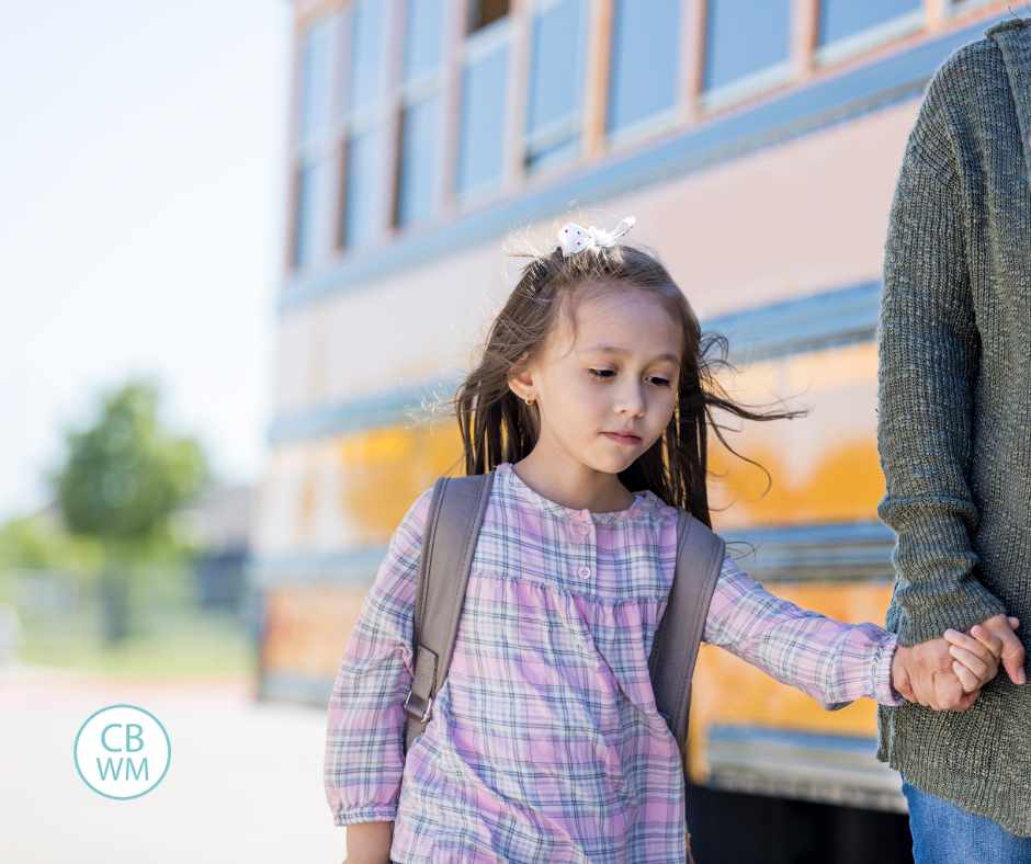 Girl walking in front of a bus looking nervous and holding her mom's hand