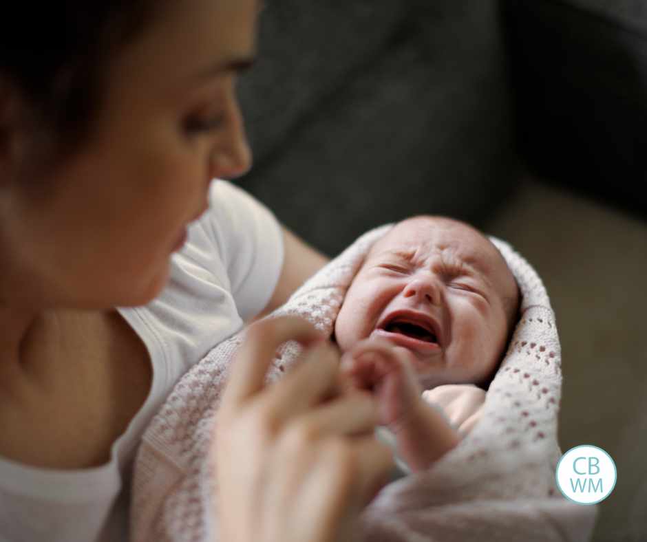 Mom holding a crying newborn wrapped in a blanket