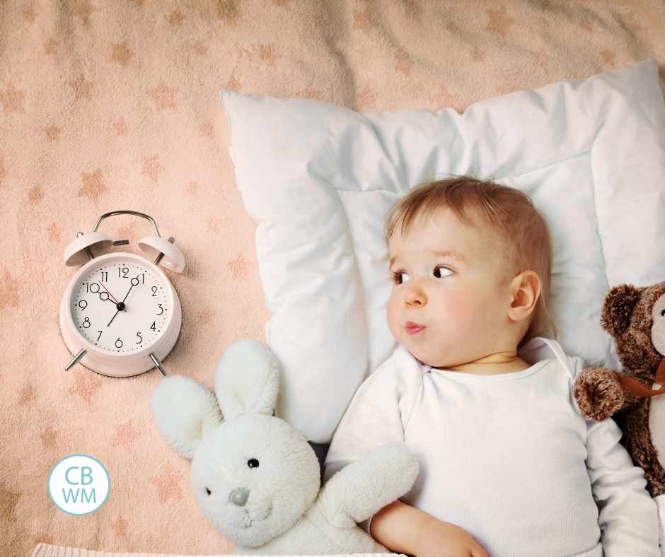 Baby lying in bed side-eyeing a clock