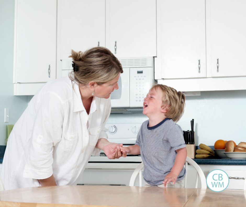 Toddler standing on a chair crying while mom attends to him