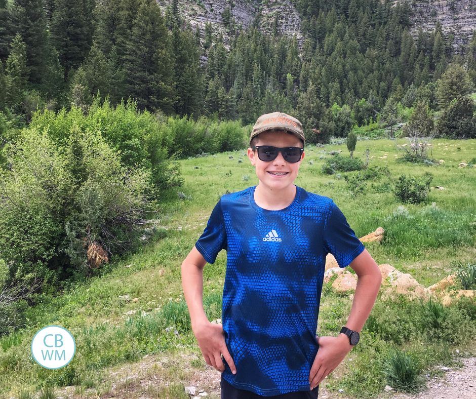 Brayden with a ball cap and sunglasses standing outside in the mountains