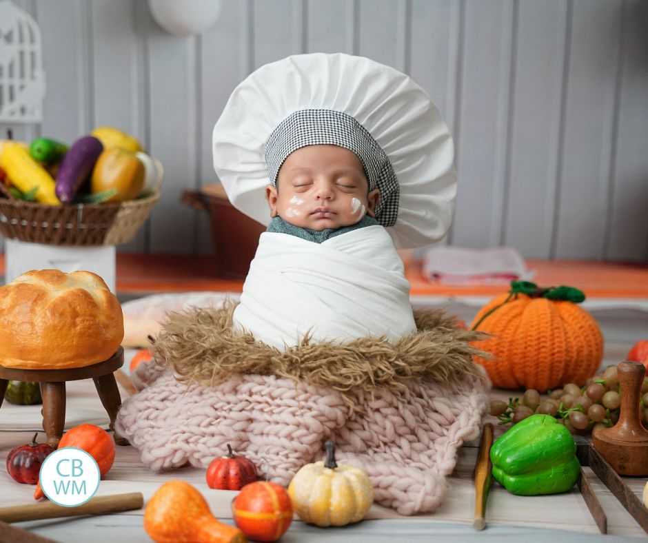 Sleeping baby dressed up in chef outfit and surrounded by food